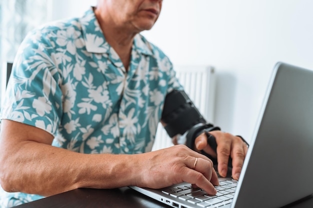 Homem com órtese de cotovelo articulado ajustável digitando no teclado do laptop