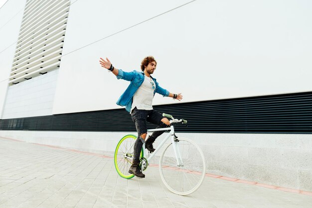 Foto homem com os braços estendidos a andar de bicicleta na rua ao lado do edifício