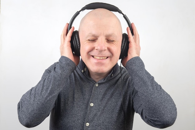 Homem com os olhos fechados ouve música com fones de ouvido em um fundo claro