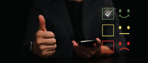 Foto homem com polegar para cima e usando telefone inteligente para dar classificação satisfeita com o ícone de rosto sorridente para avaliar o produto e serviço.