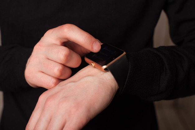 Homem com relógio inteligente em roupas pretas. Feche de mãos.