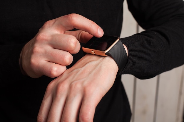 Homem com relógio inteligente em roupas pretas. Feche de mãos.