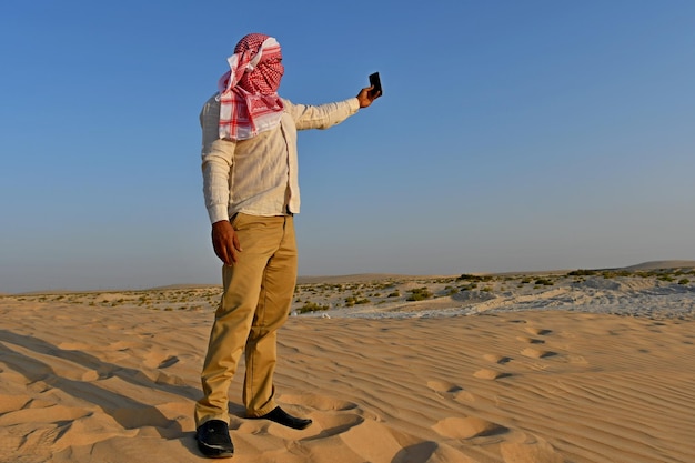 Homem com rosto coberto tirando selfie enquanto está de pé na areia na praia