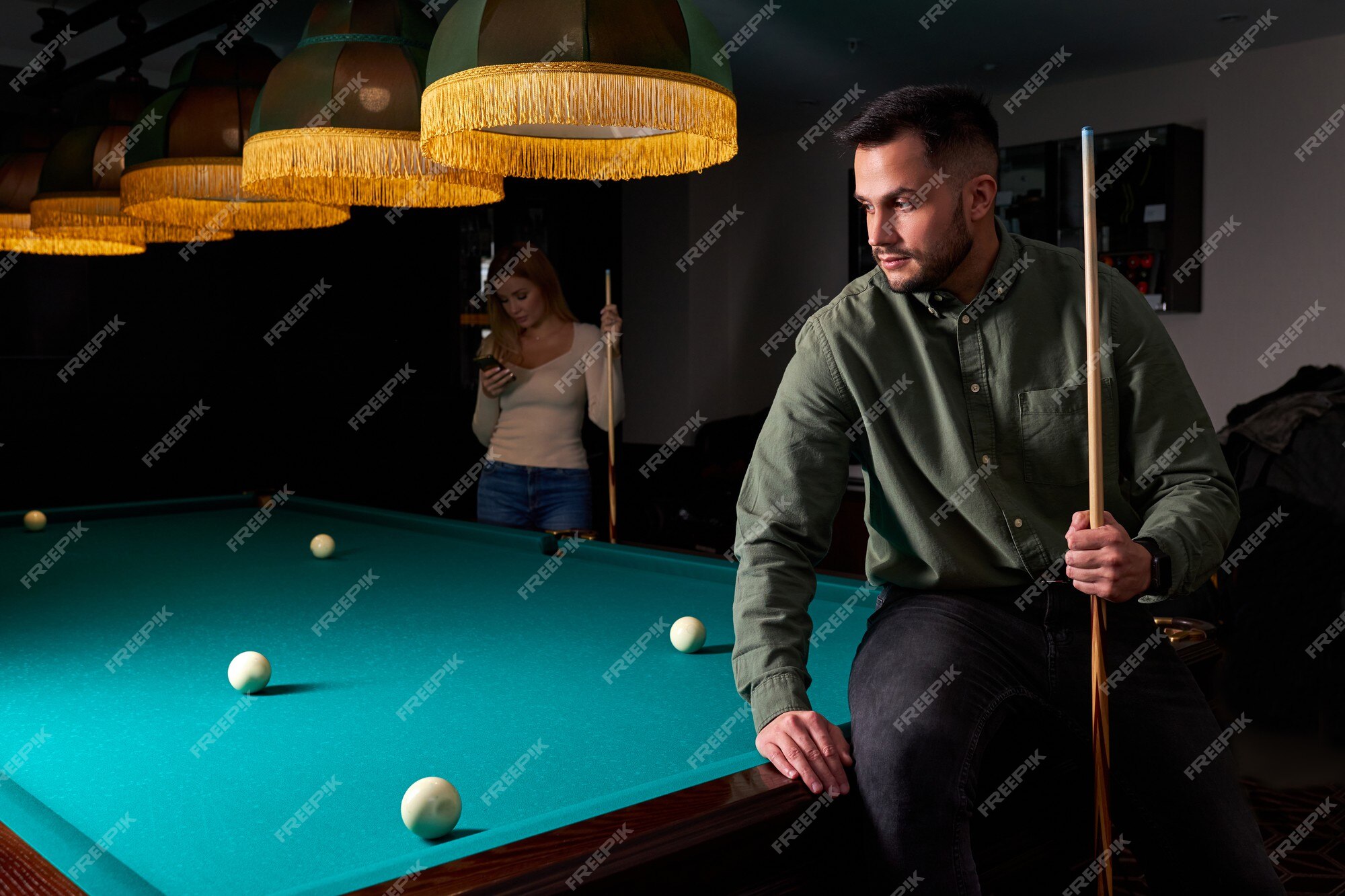 Homem com roupa casual se senta na mesa de bilhar, olhando para o jogo, o  conceito de jogo de esporte de sinuca. retrato