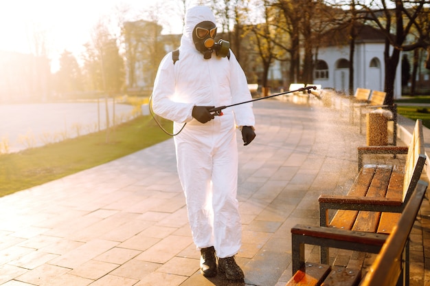 Homem com roupa de proteção contra vírus e máscara desinfeta locais públicos com produtos químicos em spray. Covid19.