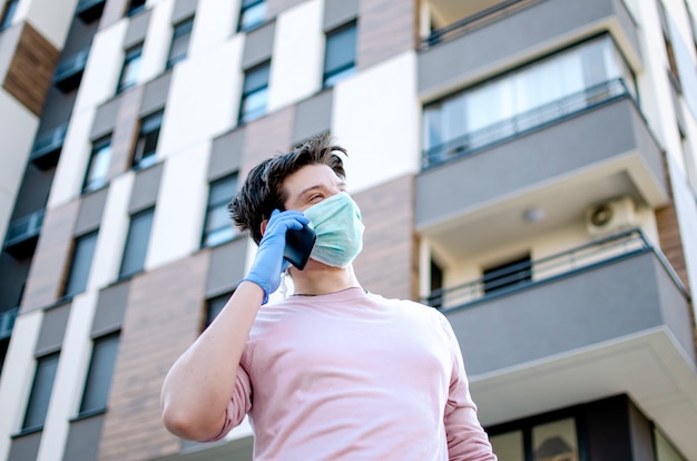 Foto homem com roupa médica protetora usando telefone celular andando na cidade street.guy vestindo luvas e máscara de segurança fora