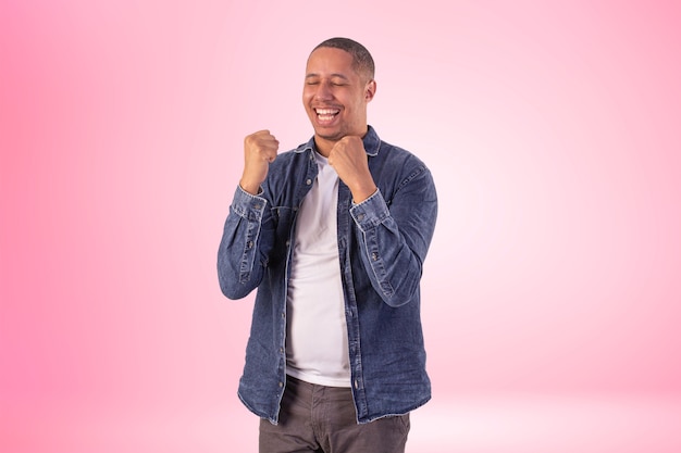 Homem com roupas curtas, vestindo camisa jeans, camiseta branca e calça marrom em foto de estúdio em um fundo com luzes.