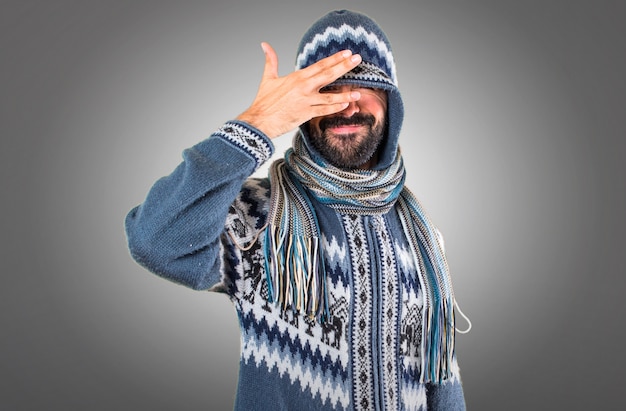 Homem com roupas de inverno cobrindo os olhos no fundo cinza