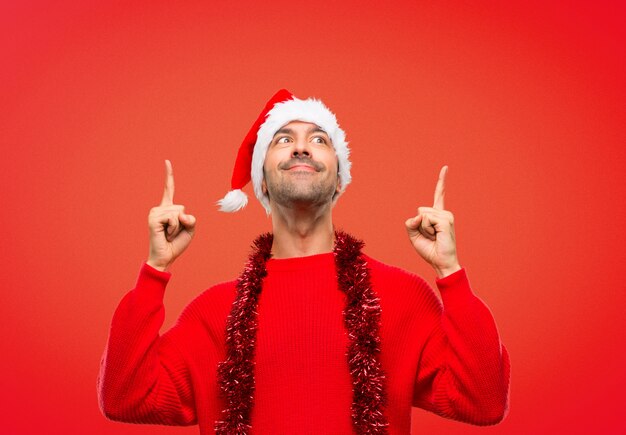 Foto homem com roupas vermelhas, comemorando as férias de natal, apontando com o dedo indicador