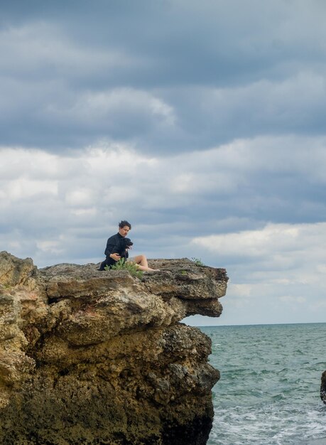 homem com seu cachorro sentado em uma baía olhando o mar