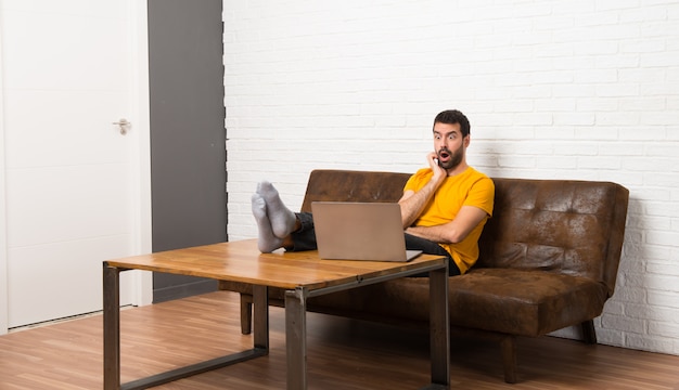 Homem com seu laptop em um quarto surpreso e chocado ao olhar para a direita