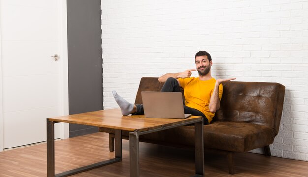 Homem com seu laptop em uma sala segurando copyspace imaginário na palma da mão para inserir um anúncio