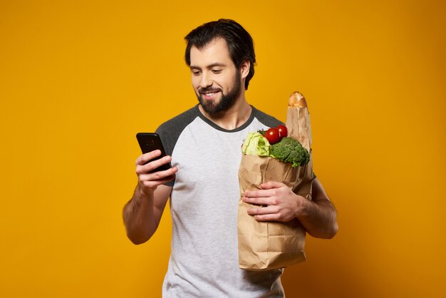 Homem com smartphone detém o saco de papel com produtos frescos.