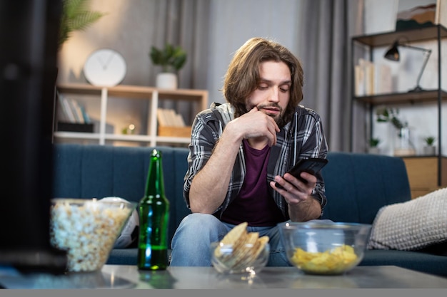 Homem com smartphone no sofá assistindo jogo de futebol