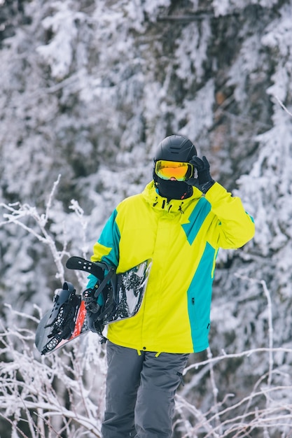 Homem com snowboard caminhando por uma colina coberta de neve, atividades de inverno