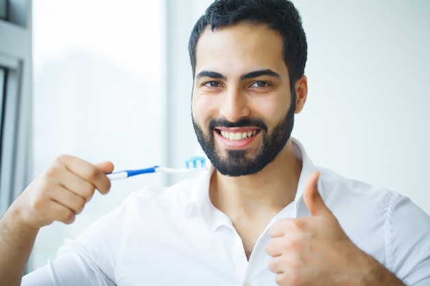 Homem com sorriso lindo, dentes brancos saudáveis e escova de dentes