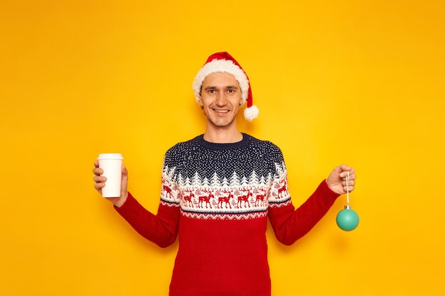 homem com suéter de Natal com chapéu de Papai Noel vermelho de rena e brinquedo de árvore de ano novo na mão