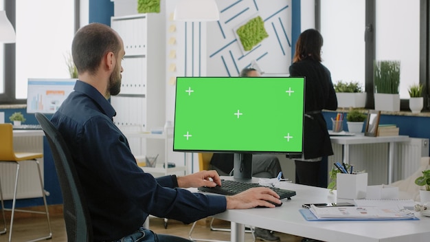 Homem com trabalho de escritório, trabalhando no computador com tela verde para projeto de tecnologia. homem de negócios usando monitor com modelo de maquete e fundo isolado para chroma key no display.
