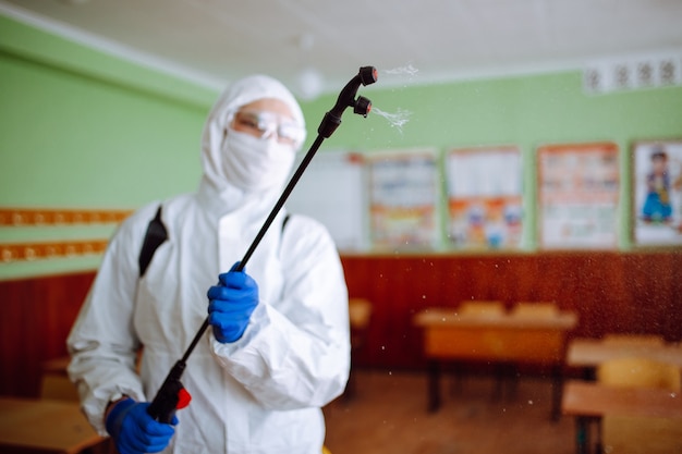 Homem com traje de proteção desinfetando uma sala de aula