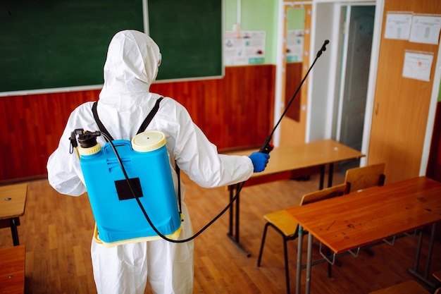 Homem com traje de proteção desinfetando uma sala de aula