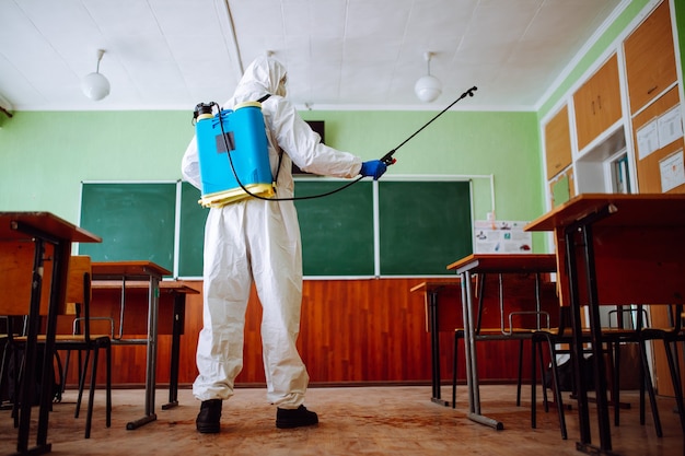 Homem com traje de proteção desinfetando uma sala de aula