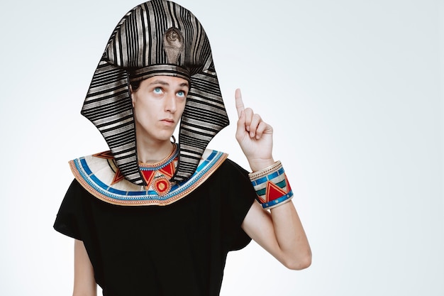Homem com traje egípcio antigo, olhando para cima com uma cara séria apontando com o dedo indicador para cima no branco