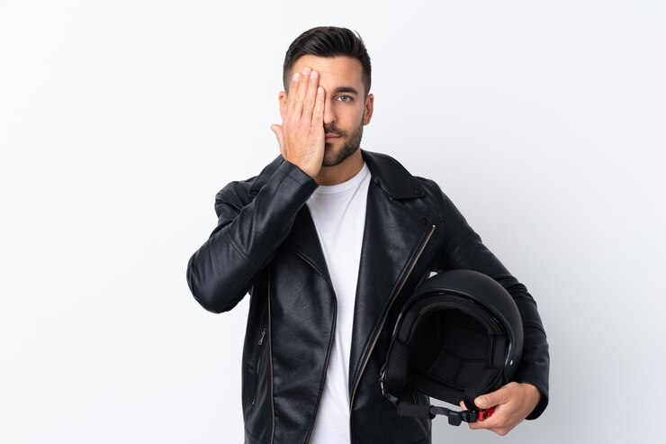 Foto homem com um capacete de moto cobrindo um olho com a mão
