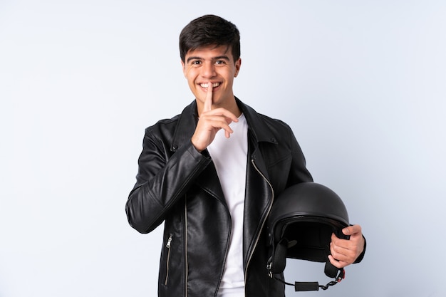 Homem com um capacete de moto na parede azul, fazendo o gesto de silêncio