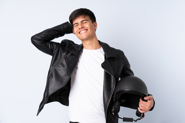 Homem com um capacete de moto sobre parede azul rindo