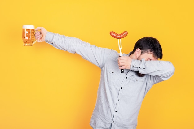 Homem com um copo de cerveja e linguiça grelhada em pose de dança.