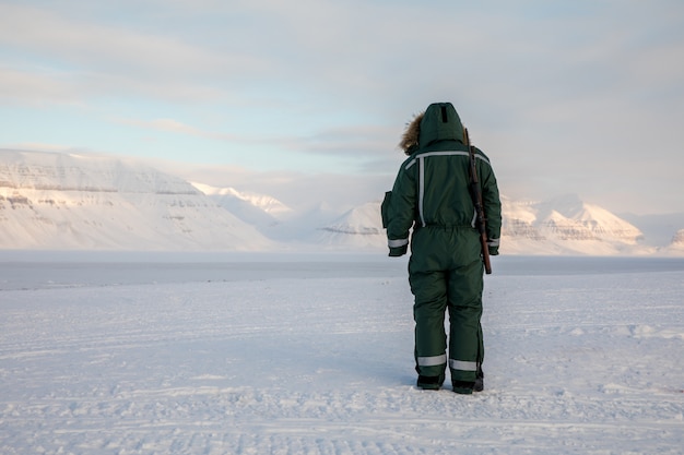 Homem com um rifle tem vista para o horizonte na paisagem ártica em svalbard