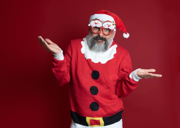 Homem com um suéter de Natal com óculos de festa espalhando surpresa no vermelho