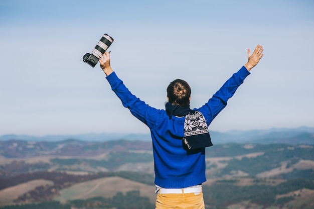 Homem com uma câmera à beira de um penhasco com vista para as montanhas abaixo