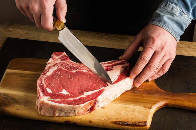 Homem com uma faca na mão cortando um bife de vitela em uma tábua de cozinha de madeira