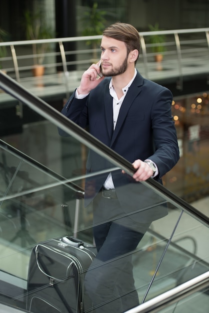 Homem com uma mala de viagem que fala no telefone.