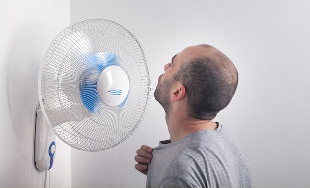 Homem com ventilador elétrico em casa