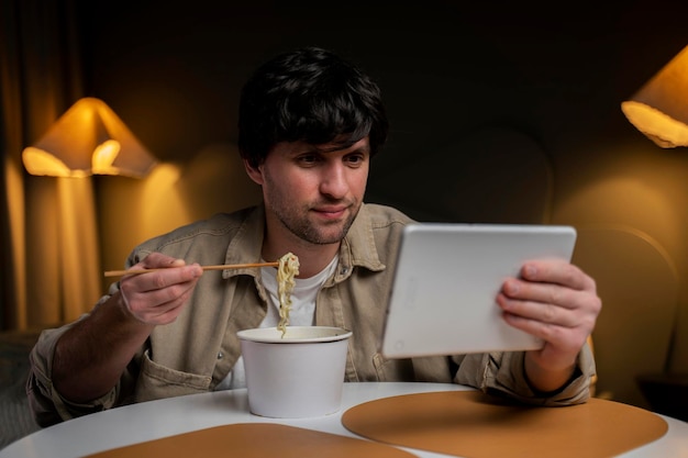 Homem come macarrão chinês enquanto navega e usa um tablet ao mesmo tempo o conceito de smartphone