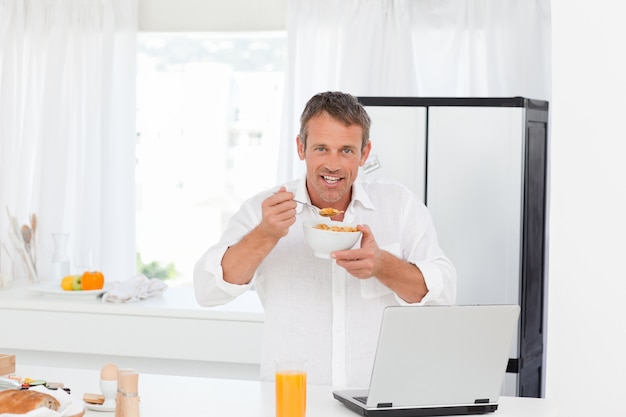 Homem comendo cereal enquanto ele está trabalhando em seu laptop