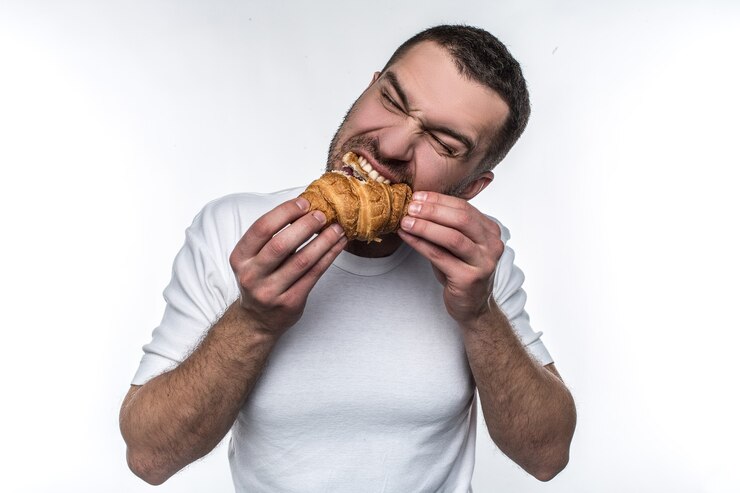 Foto homem comendo croissan. ele está mordendo com força. ele gosta dessa sobremesa francesa. isolado em fundo branco