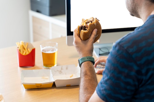 Homem comendo fast food enquanto trabalhava em seu escritório em frente ao computador