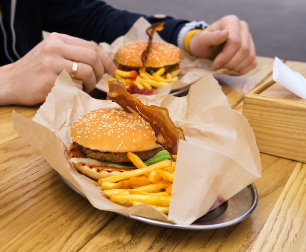 Homem comendo hambúrguer com bacon com batatas fritas e bebendo chá. comida rápida de rua.