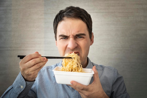 Homem comendo macarrão instantâneo enquanto trabalhava no escritório Almoço no escritório junk food sem gosto