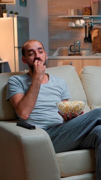 Homem comendo pipoca e assistindo TV, desfrutando de lanche da meia-noite