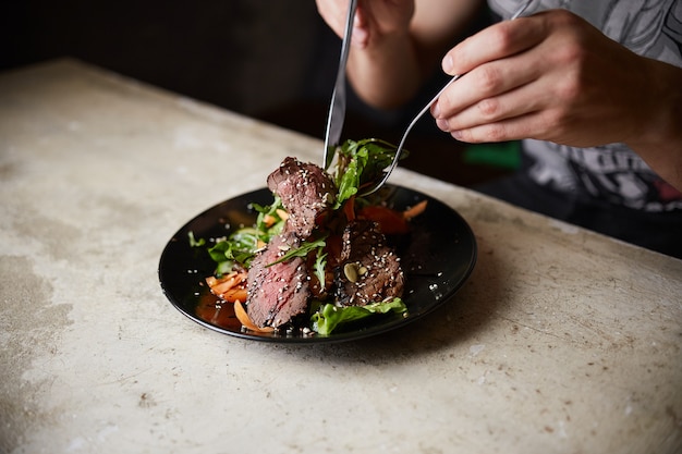 Homem comendo Salada de Bife com Carne Grelhada; Rúcula; cenoura e sementes. Comida saudável