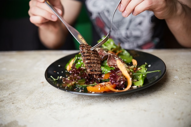 Homem comendo Salada de Bife com Carne Grelhada; Rúcula; cenoura e sementes. Comida saudável