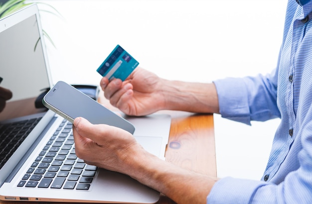 Homem comprando e pagando com celular, laptop e cartão de crédito. Copie o espaço.