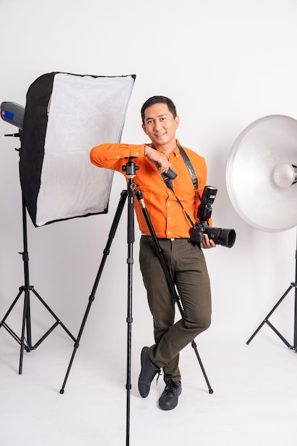 Homem confiante em pé apoiado no tripé segurando a câmera com equipamento fotográfico nas costas isoladas