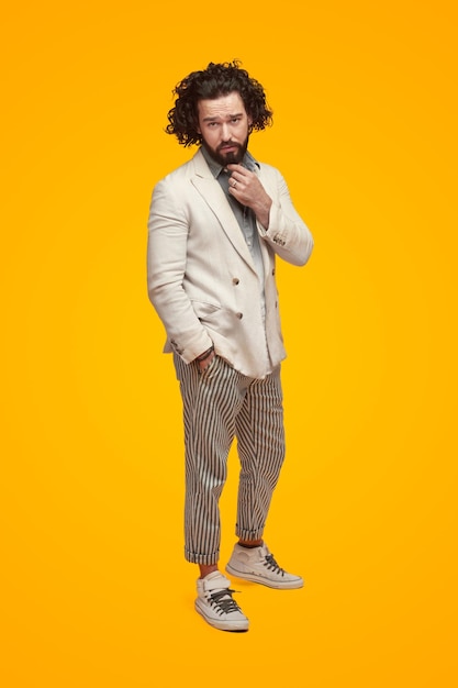 Homem confiante em roupa hipster tocando barba no estúdio
