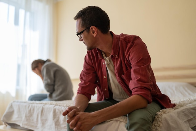 Homem confuso olha para menina chorando sentada no lado oposto da cama após conversa desagradável