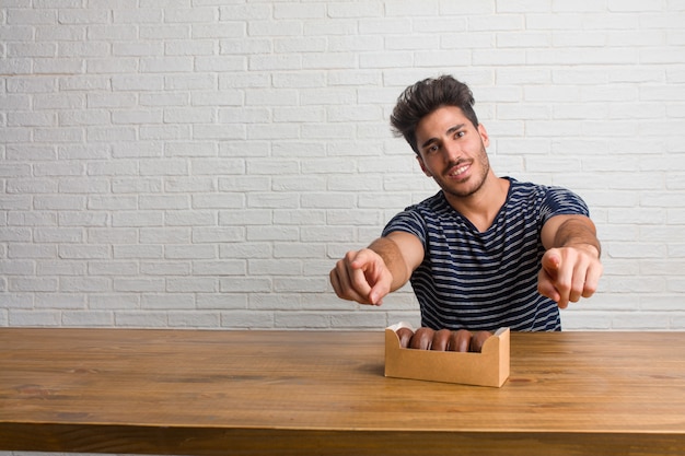 Homem considerável e natural novo que senta-se em uma tabela alegre e que sorri apontando à parte dianteira